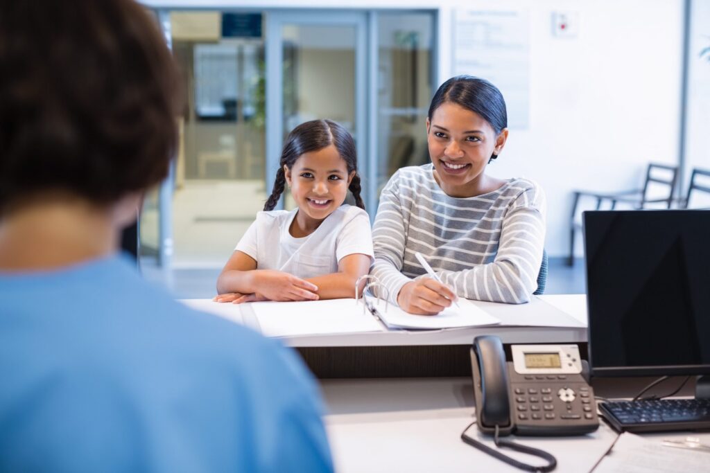 A mother and daughter smiling at the receptionist as they check in for their appointment.