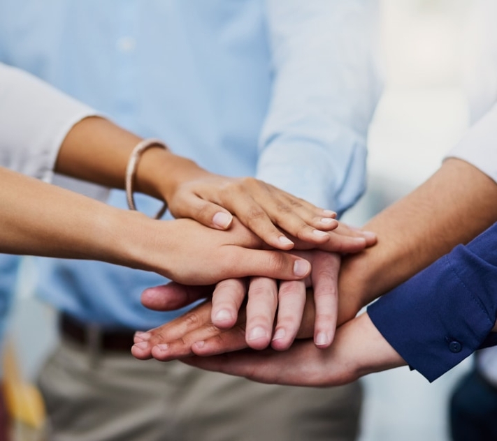 Group of people placing their hands together in a teamwork gesture.